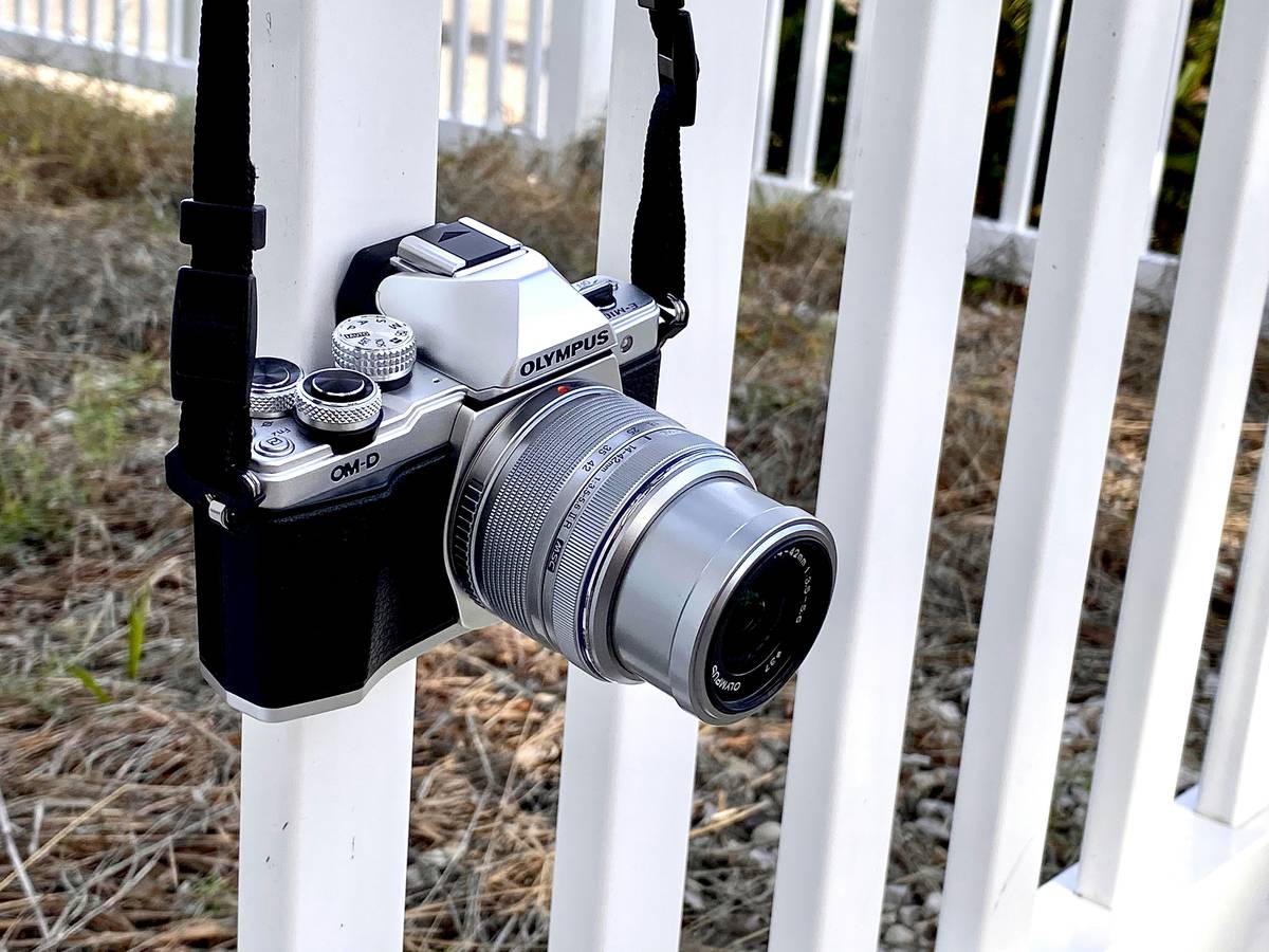 A hiker adjusting their DSLR camera amidst snow-covered mountains.