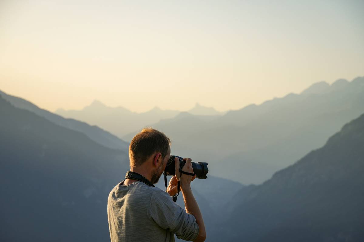 A hiker adjusting their lightweight DSLR while standing near a waterfall.