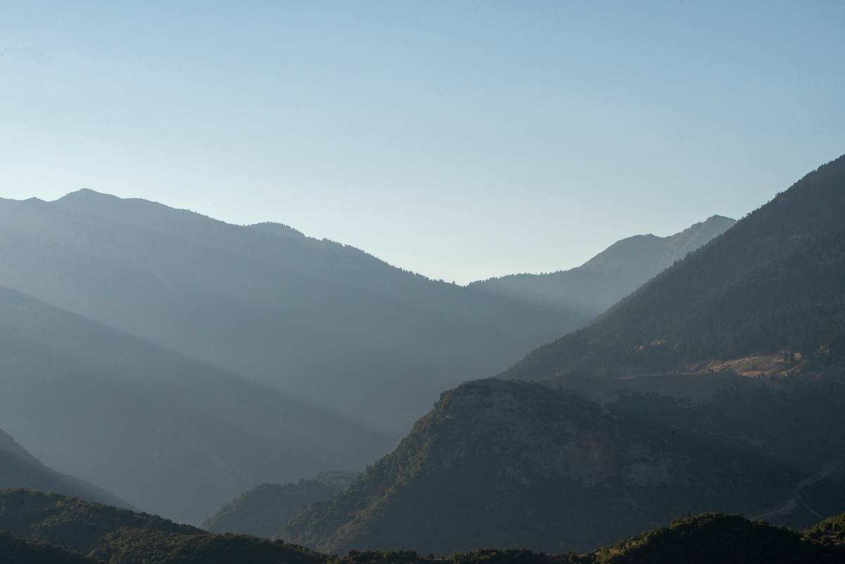 A hiker holding a DSLR camera with a wide field lens pointing toward a vast mountain vista