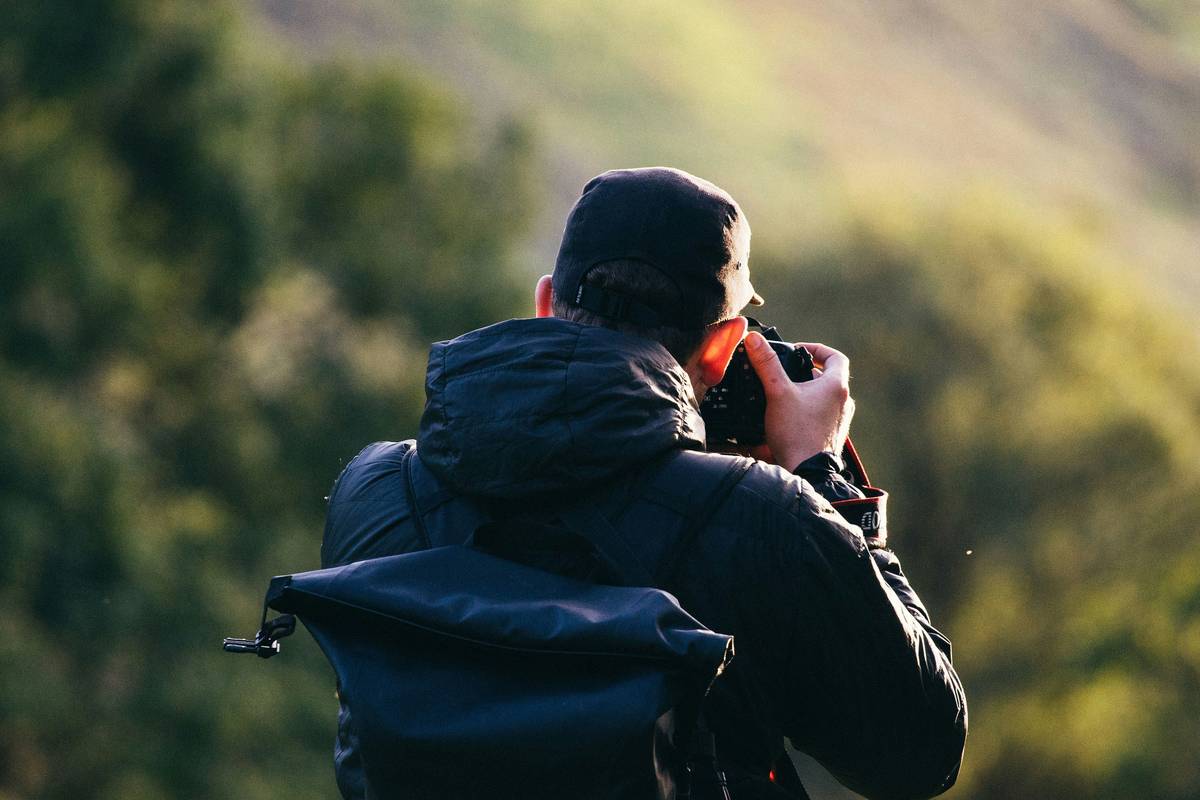 A hiker holding a camera with a stabilized nature lens amidst lush greenery