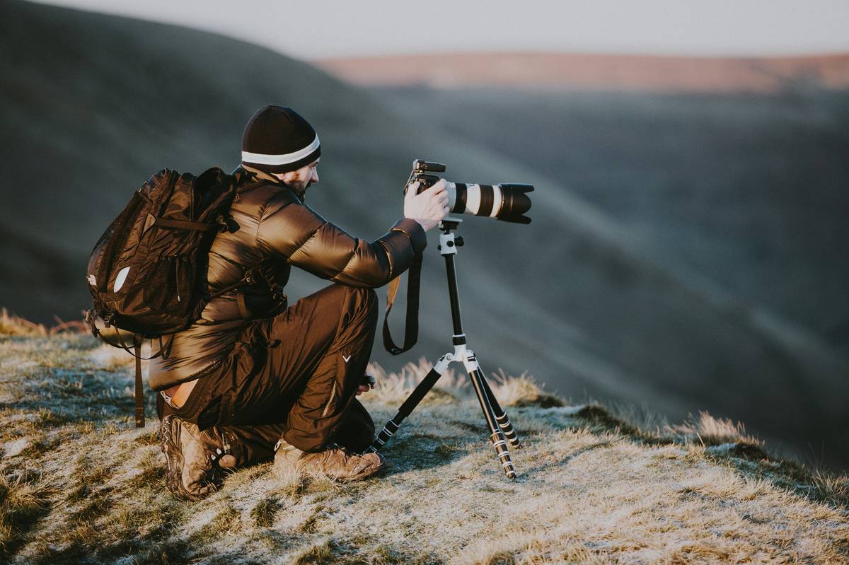 A hiker wearing a helmet-mounted 360 degree adventure camera while traversing a scenic mountain trail.